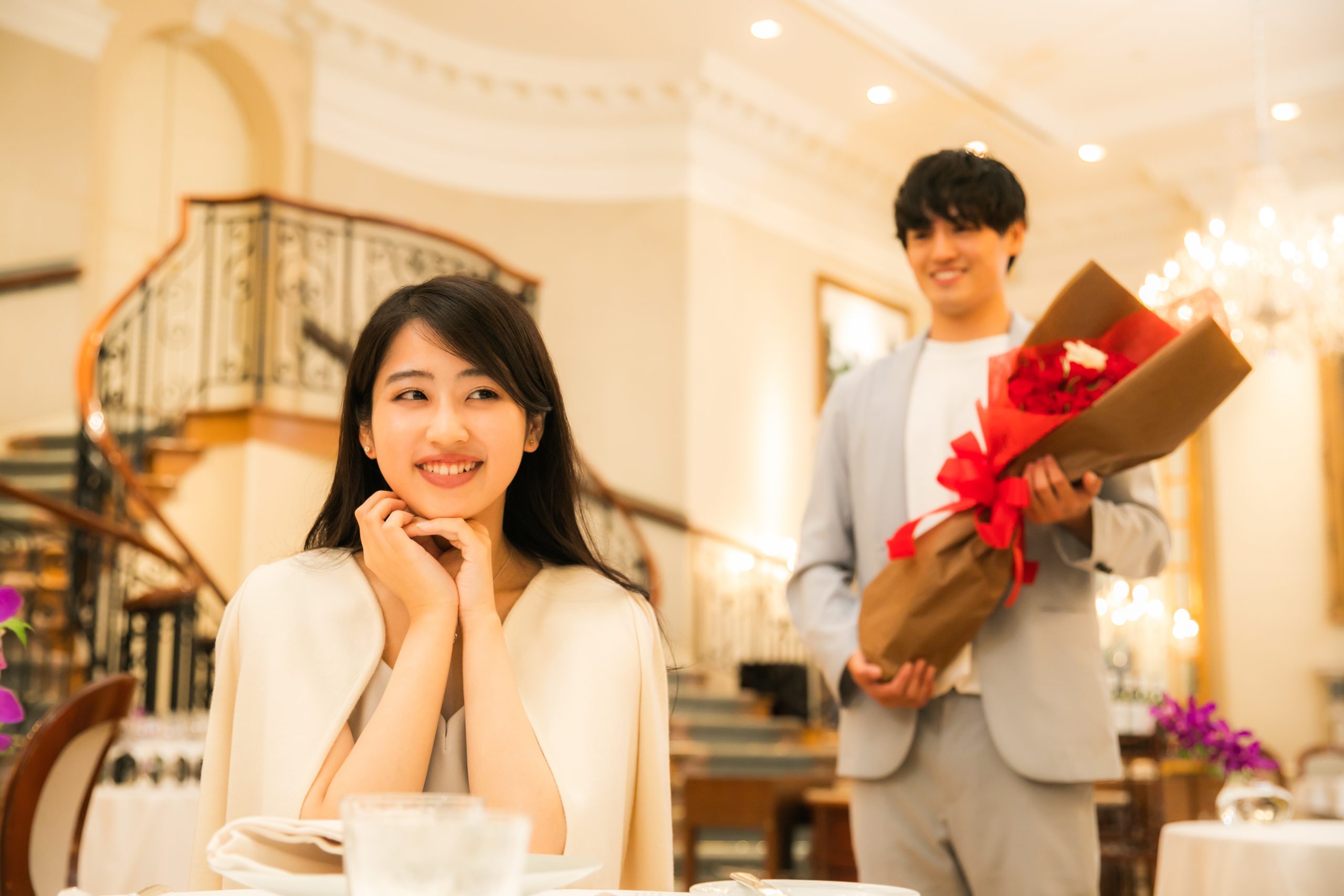 レストランでのプロポーズを待つ女性と花束を持って近づく男性
