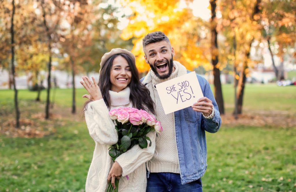 プロポーズが成功し花束を抱えて嬉しそうな女性とその横でshe said yes!と書かれた紙を持ち上機嫌の男性