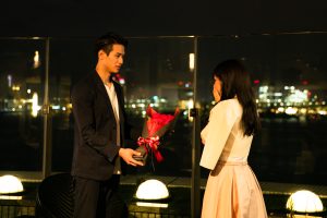 夜景の見える場所でバラの花束を出してプロポーズする男性