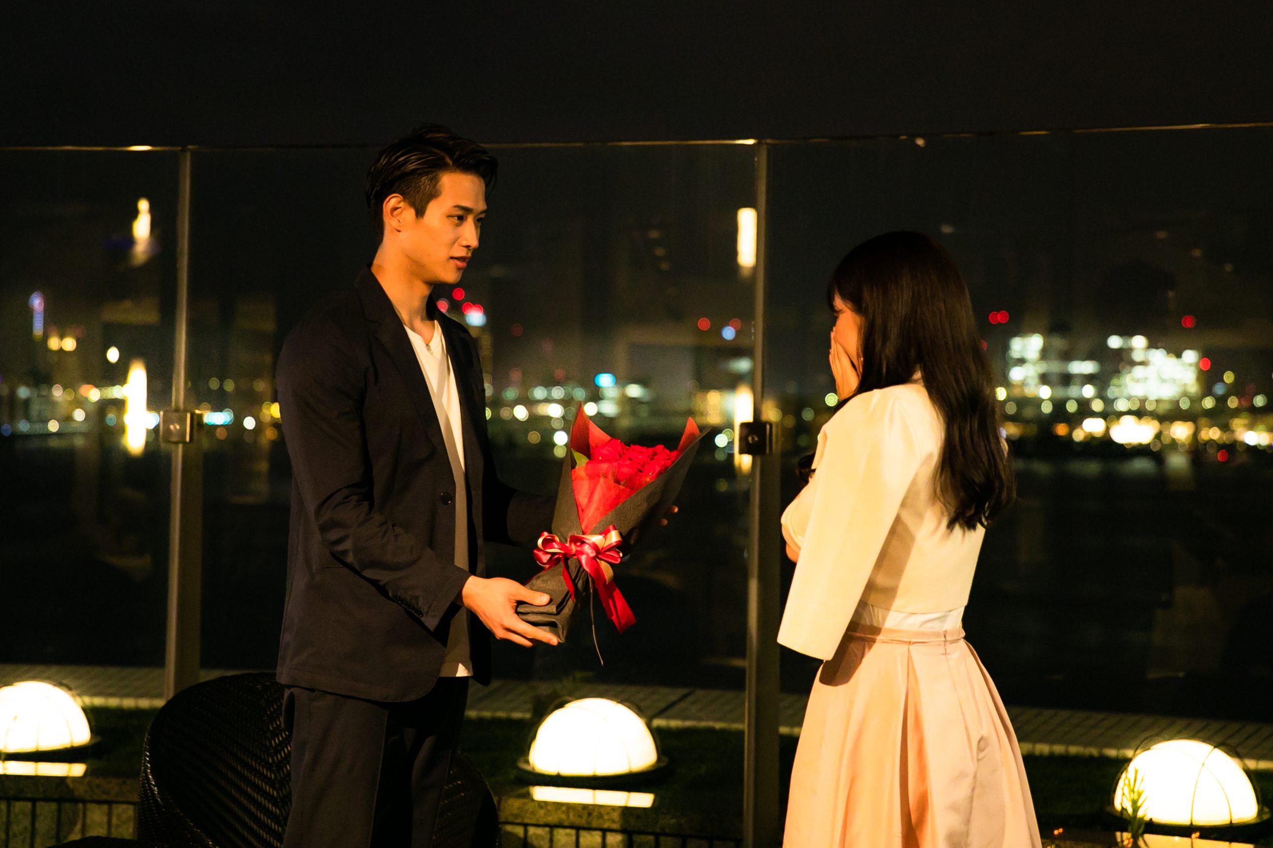 夜景の見える場所でバラの花束を贈ってプロポーズする男性