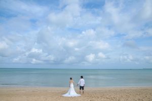 ハワイのビーチでハネムーンフォトを撮るカップルの後ろ姿