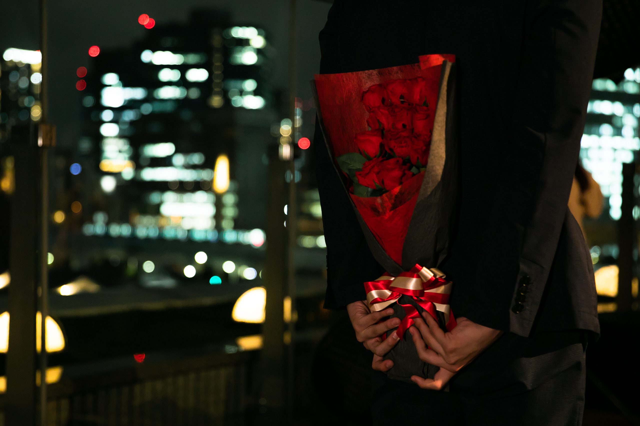 プロポーズ用のバラの花束を体の後ろで隠すように持つ男性