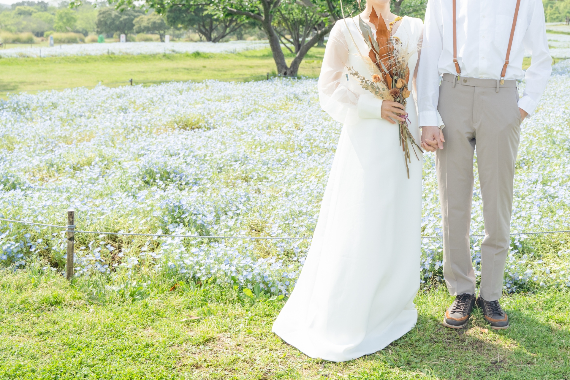 花畑で手をつなぎ、ウェディングフォト撮影する新郎新婦